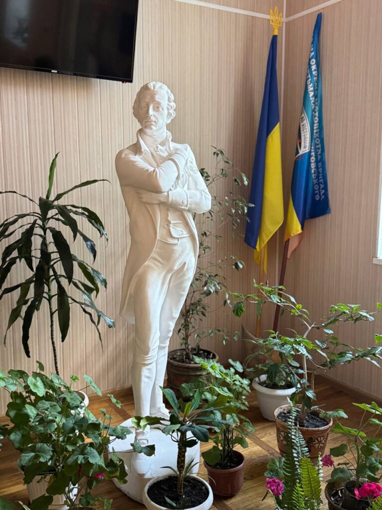 Скульптура композитора Дмитра Бортнянського у Сумському фаховому коледжі мистецтв і культури серед кімнатних рослин та українських прапорів.
