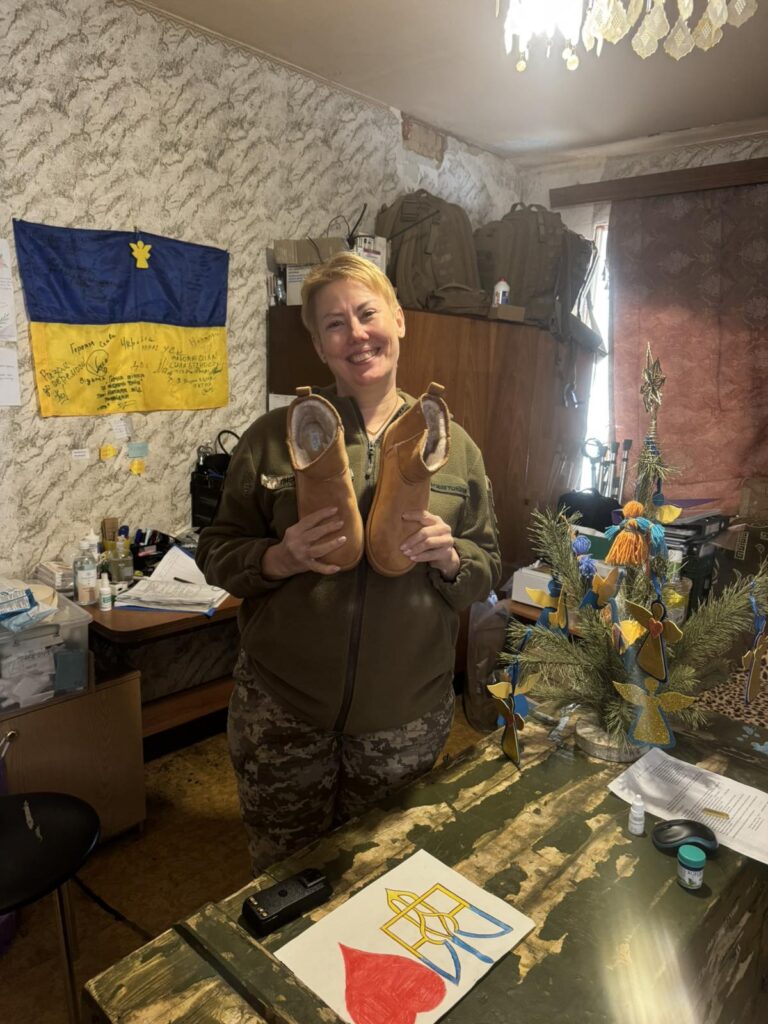 Наталія Гузь усміхається в кімнаті та тримає теплі капці, передані для військових
