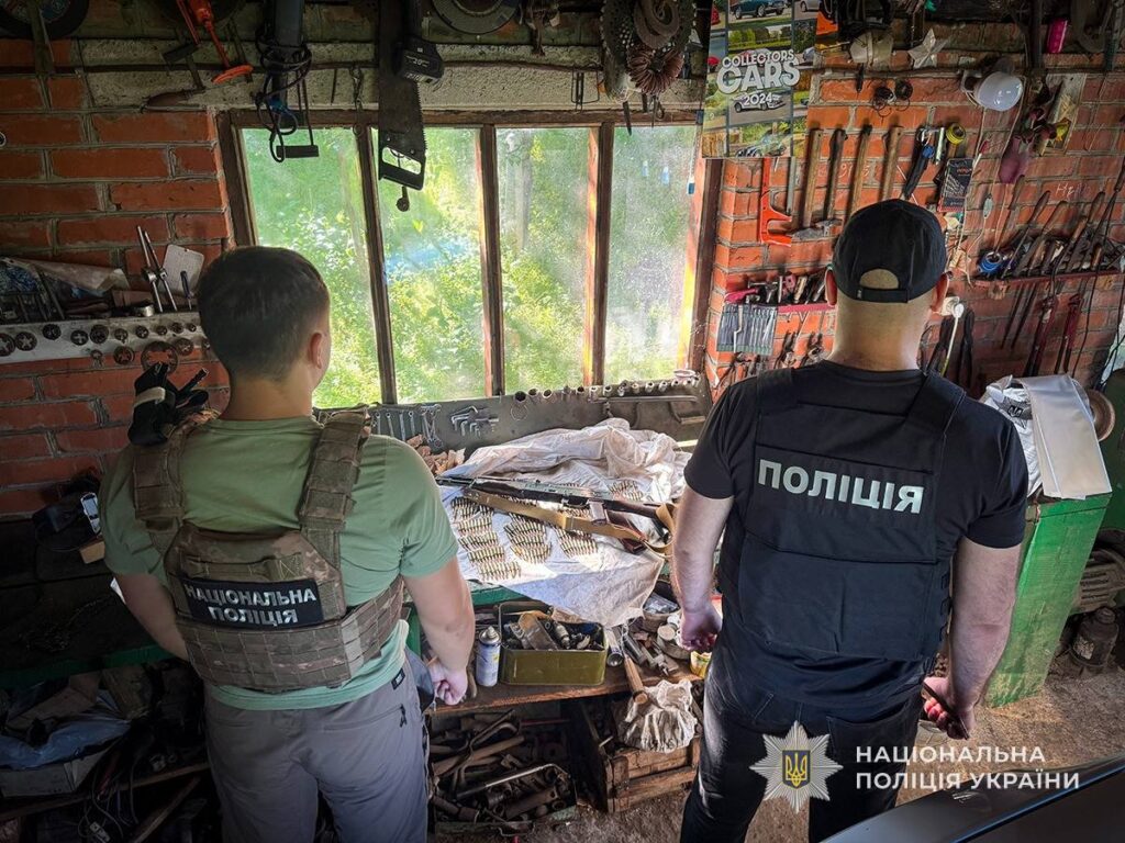 Поліцейські під час обшуку в господарському приміщенні на Охтирщині, де на столі лежать вилучені автоматична зброя та набої.